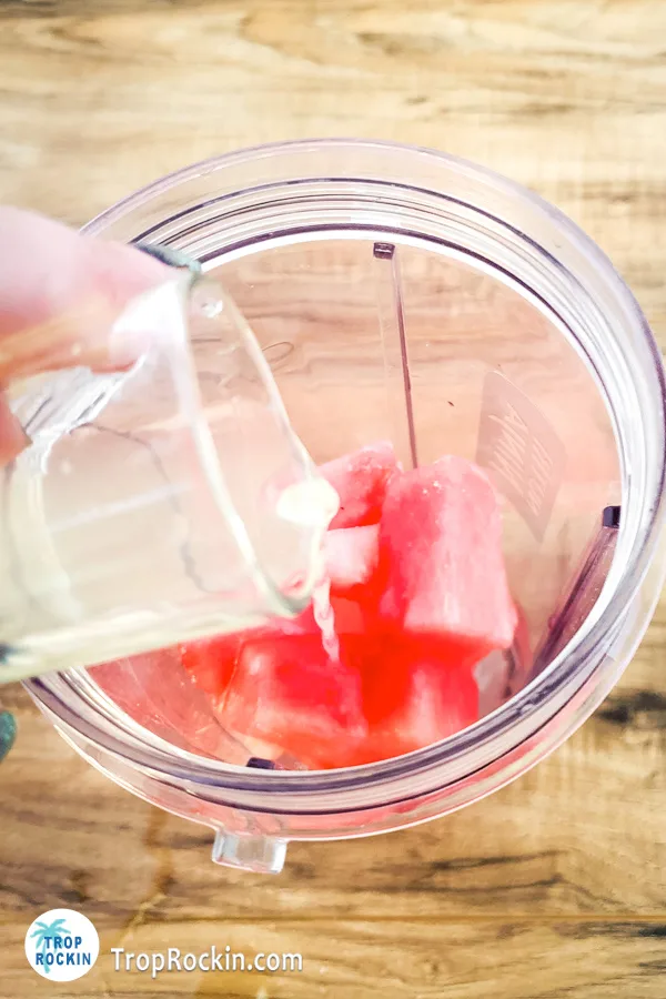 Pouring vodka and mix into blender over frozen watermelon chunks.