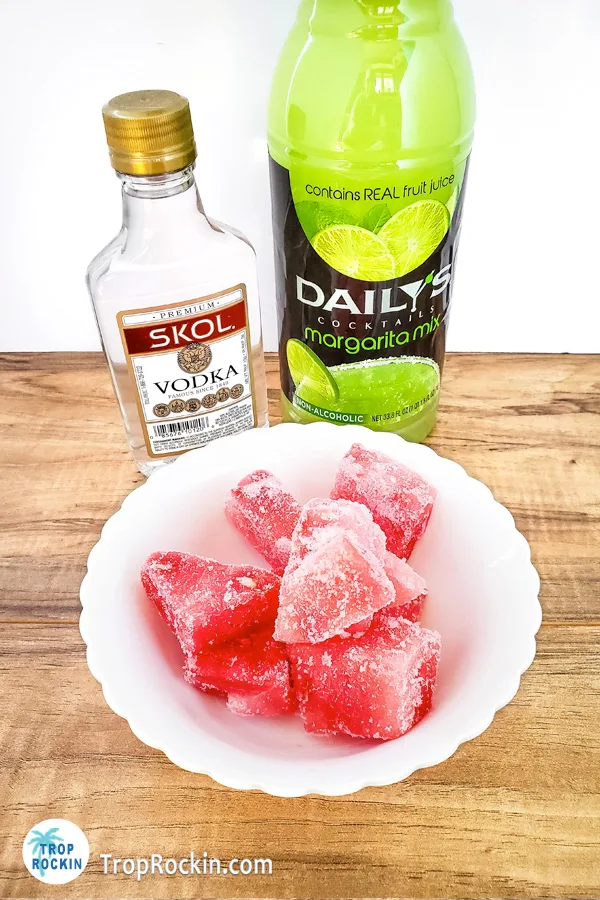 Watermelon Vodka Slushie ingredients: bowl of frozen watermelon chunks with bottle of vodka and margarita mix.