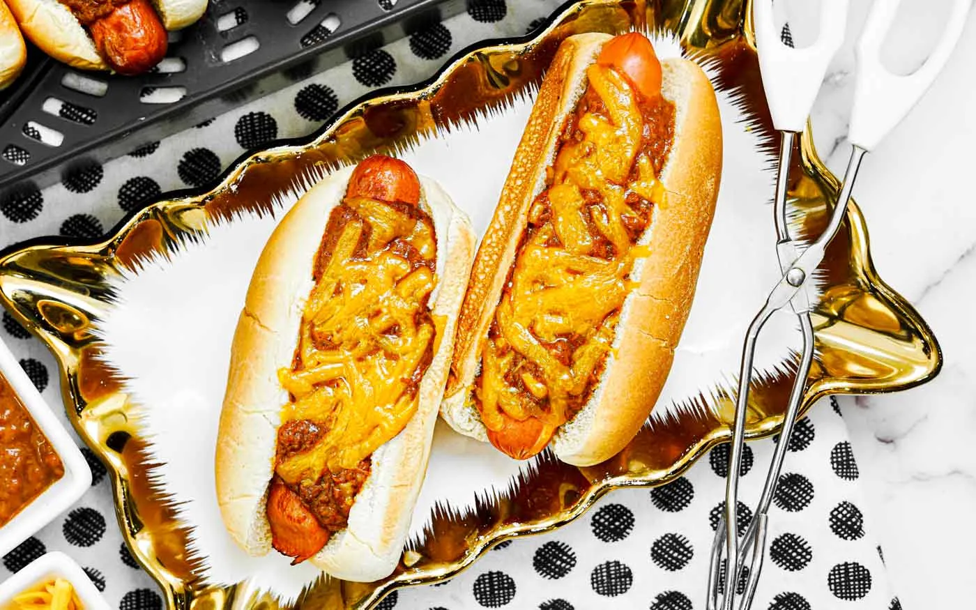 Air fryer hot dogs with chili and cheese on a serving plate.