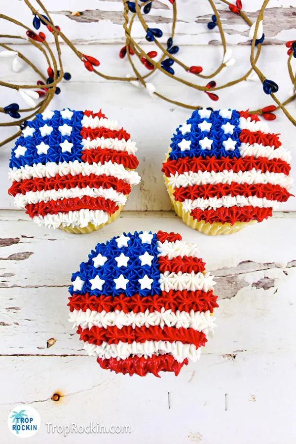 Three American Flag Cupcakes on a white wood background.
