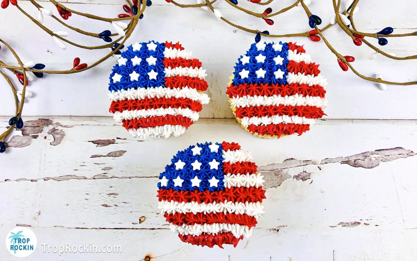 Three American Flag Cupcakes on a white wood background.