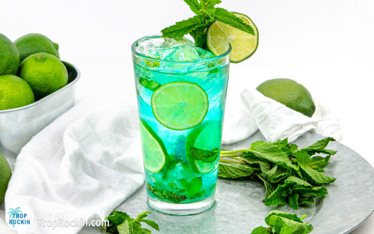 Blue Mojito drink with fresh mint leaves and fresh lime slices inside the glass with a mint sprig and lime wheel for garnish.