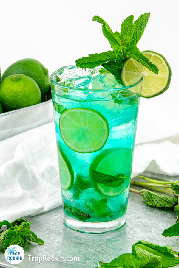 Blue Mojito drink with fresh mint leaves and fresh lime slices inside the glass with a mint sprig and lime wheel for garnish.