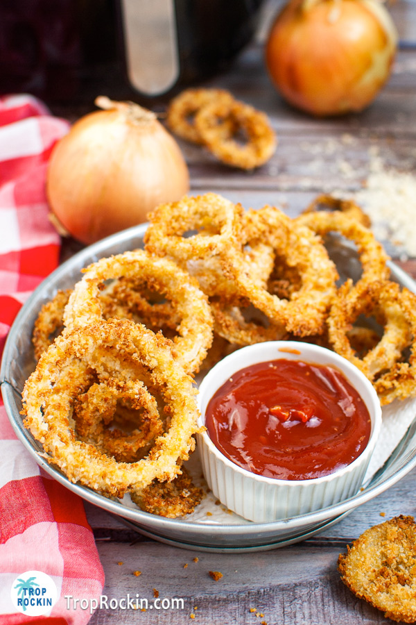 Tin tray filled with air fried onion rings with a ramekin of ketchup.