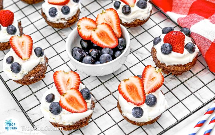 4th of July Brownie Bites topped with whipped cream, blueberries and strawberries sitting on a cooling rack.