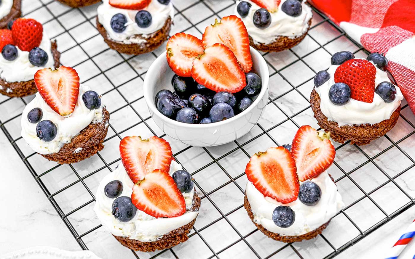 4th of July Brownie Bites with whipped topping and fresh strawberries and blueberries on top sitting on a cooling rack.