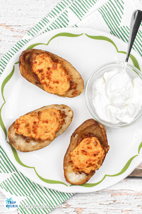 three potato skins on plate with bowl of sour cream and a spoon.