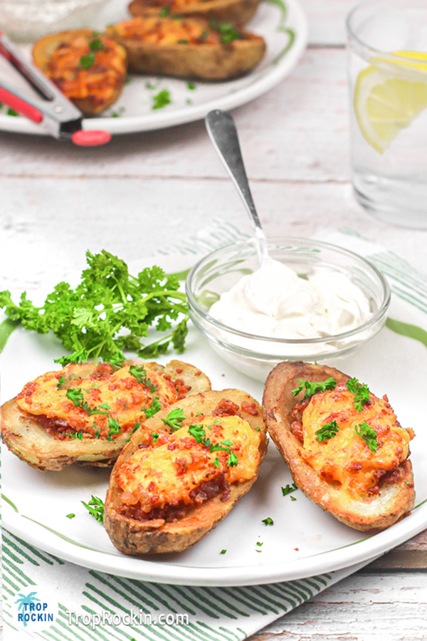 Three potato skins on a plate with bowl of sour cream with a spoon.