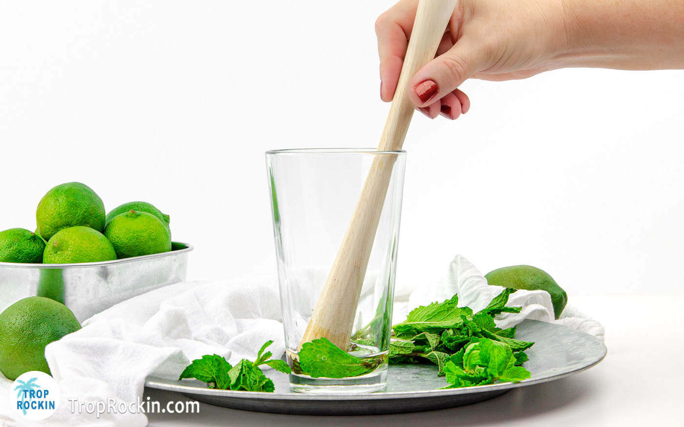 Using a muddler to bruise the mint leaves in the bottom of the glass.