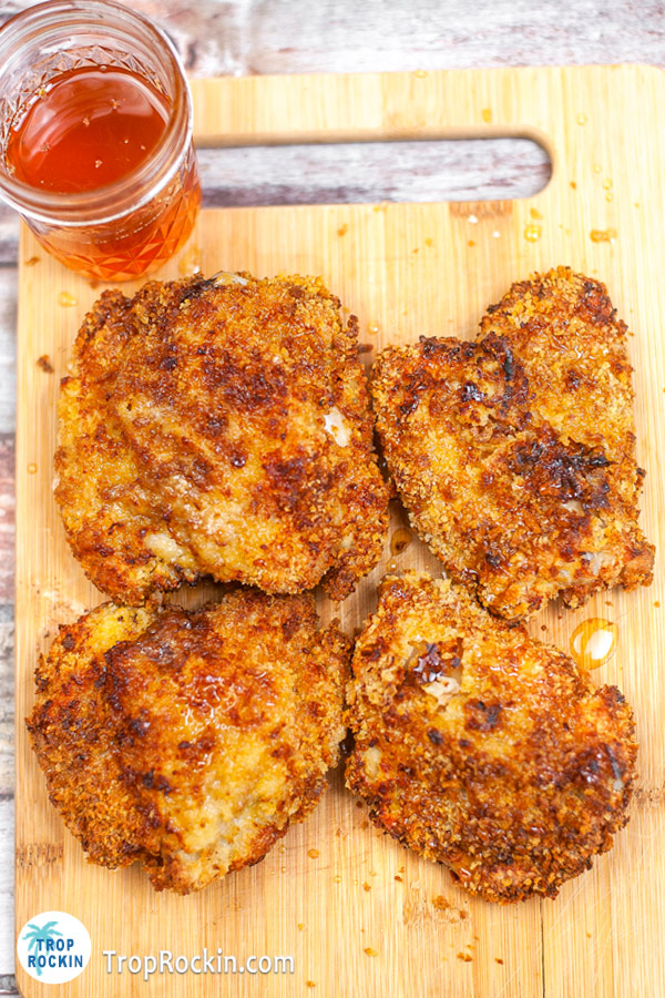 Four air fried panko chicken thighs on a cutting board with a jar of honey glaze.