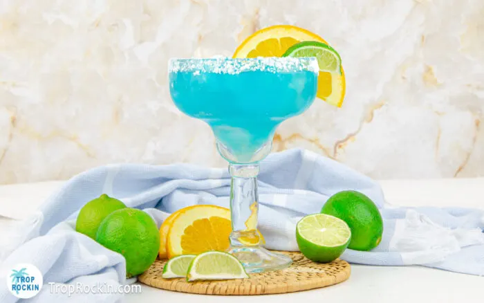 Blue margarita with salted rim and lime wedge and orange slice for garnish.