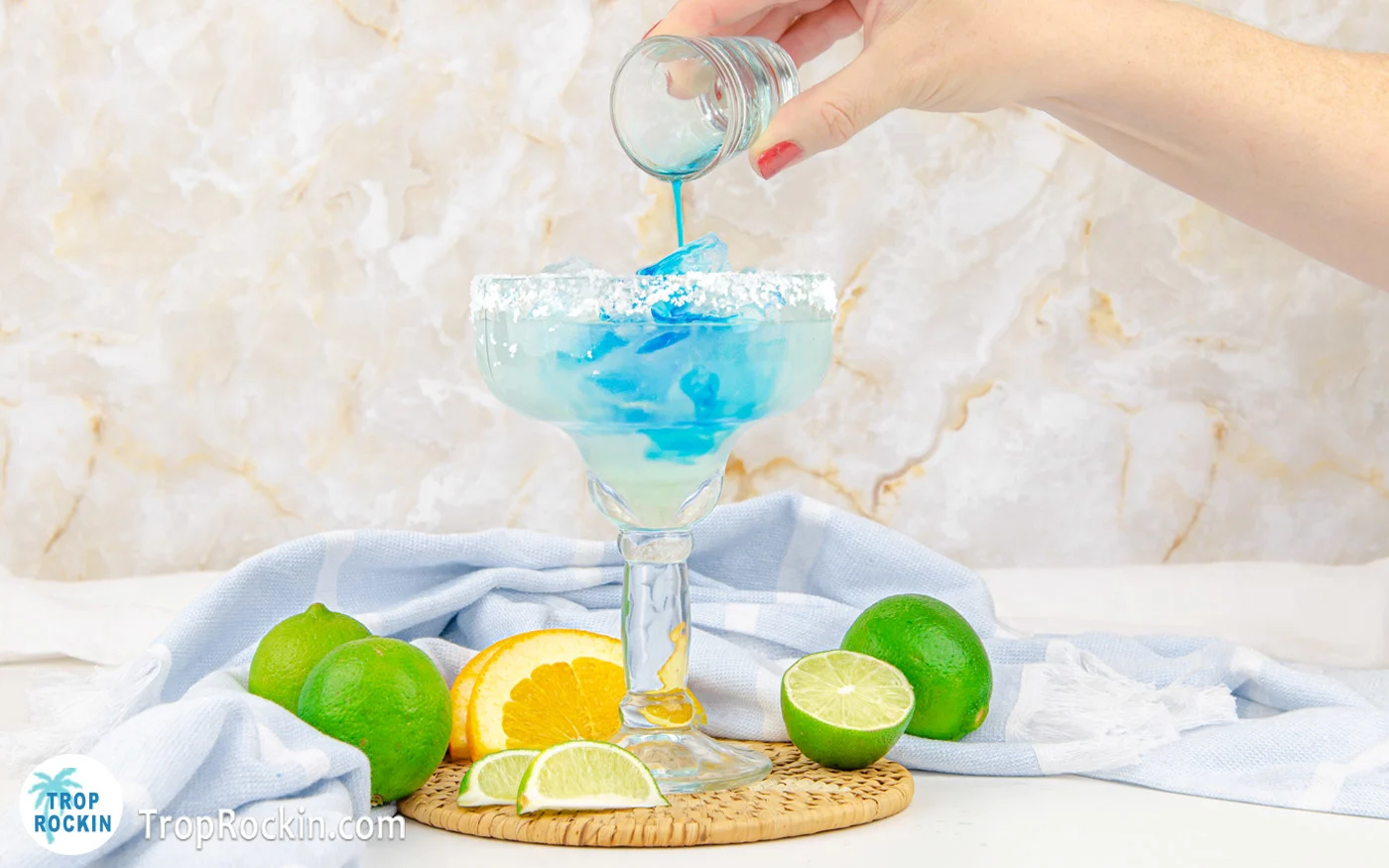 Pouring blue curacao into margarita glass filled with ice, lime juice and tequila.