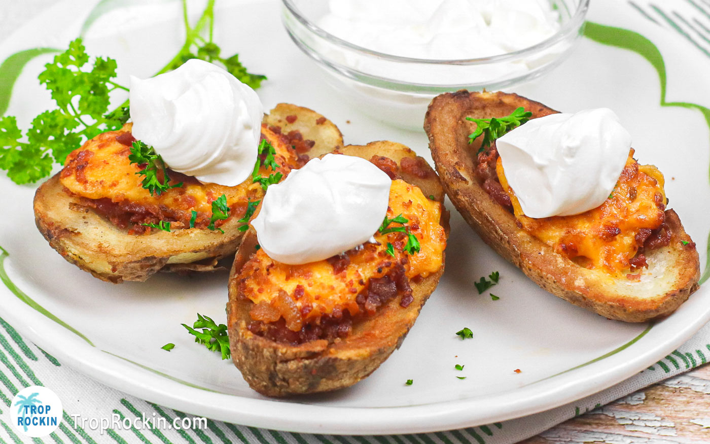 Air Fryer Frozen Potato Skins on a white plate with a dollop of sour cream on top of each one and a small bowl of sour cream on the side.