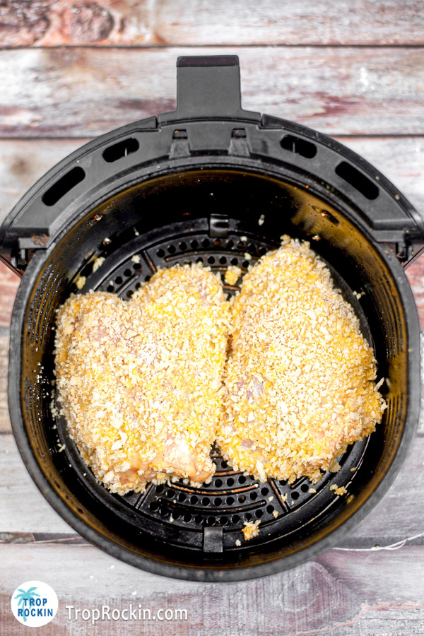 Two large boneless chicken breasts coated in flour, cornstarch, spices and panko breadcrumbs inside the air fryer basket.