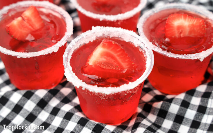 Strawberry Margarita Jello Shots with a fresh strawberry and lime slice for garnish on a green checkered napkin.