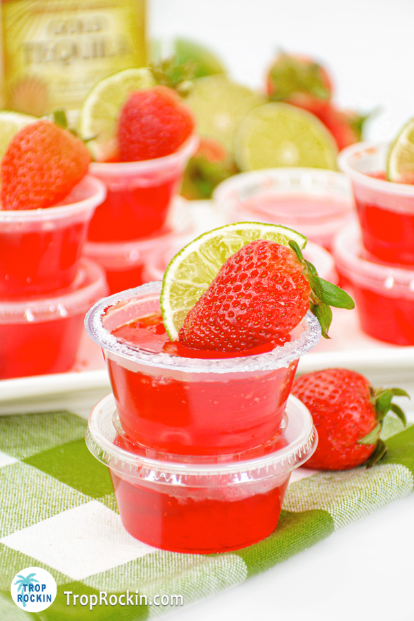 Strawberry Margarita jello shots stacked 2 high with the top jello shot including a slice of lime and strawberry for garnish on a green checkered napkin.