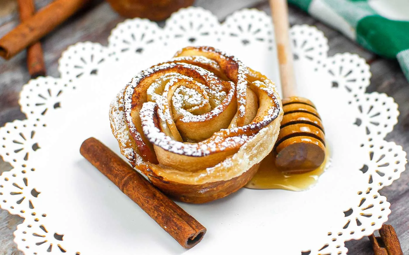 An air fried apple rose on a serving platter with a cinnamon stick and a honey dipper covered in honey.