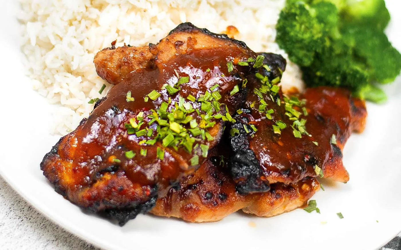 Air fried huli huli chicken on a white plate with white ride and broccoli.