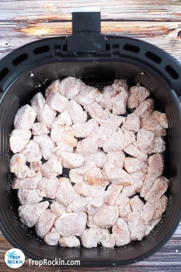 Coated chicken in the bottom of the air fryer basket.