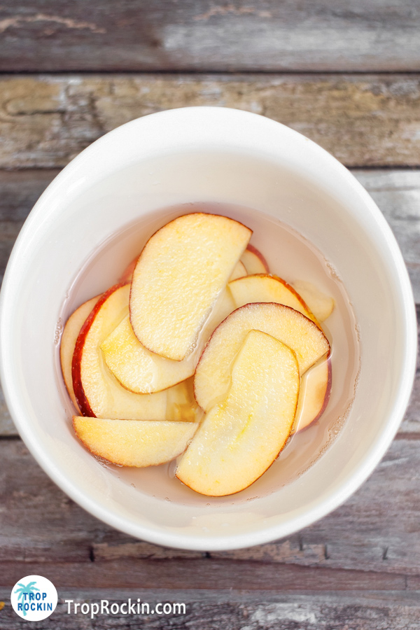 Apple slices in water and lemon juice in a white bowl.
