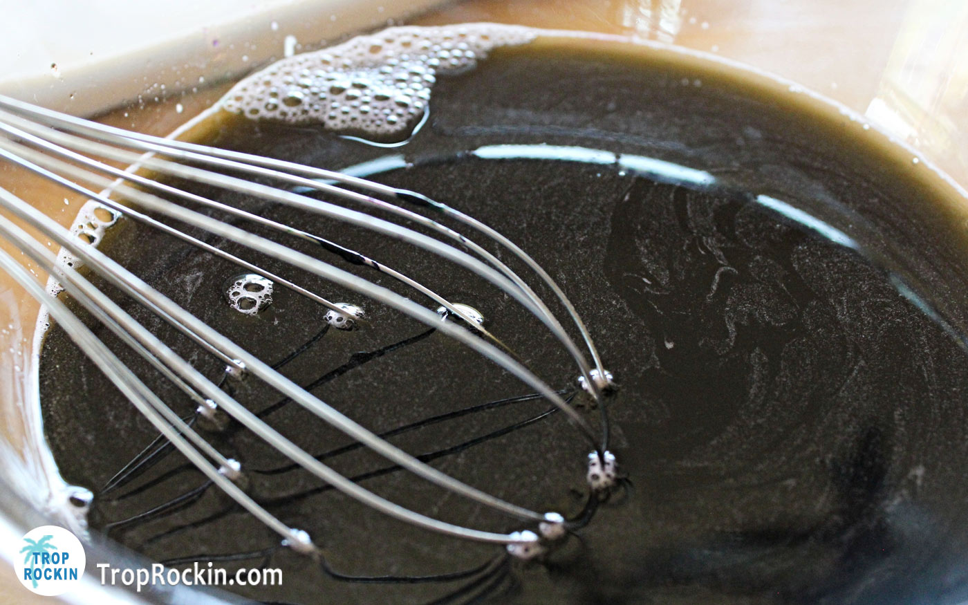 Liquid black jello in a bowl with whisk.
