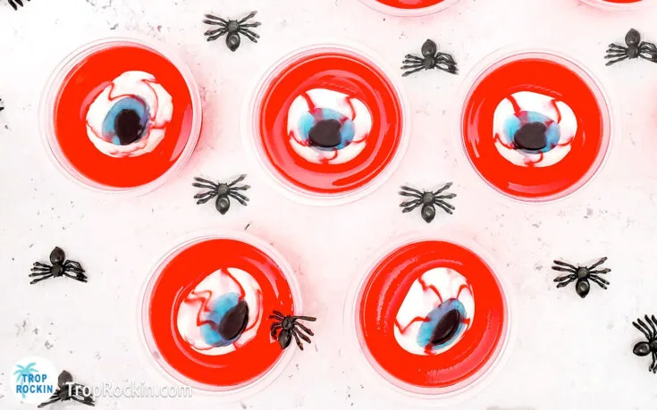 Eyeball jello shots with red jello and gummy eyeballs on top sitting on a countertop.