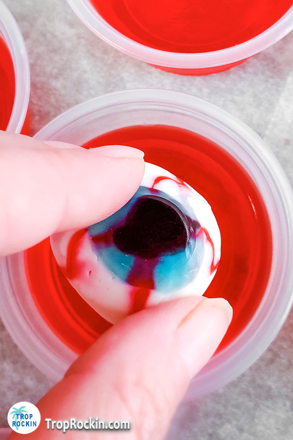 Placing a creepy gummy eyeball on top of the jello shot.