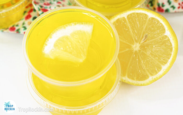 Two lemon drop jello shots stacked on top of each other on counter top. Top jello shot is garnished with a small lemon slice.