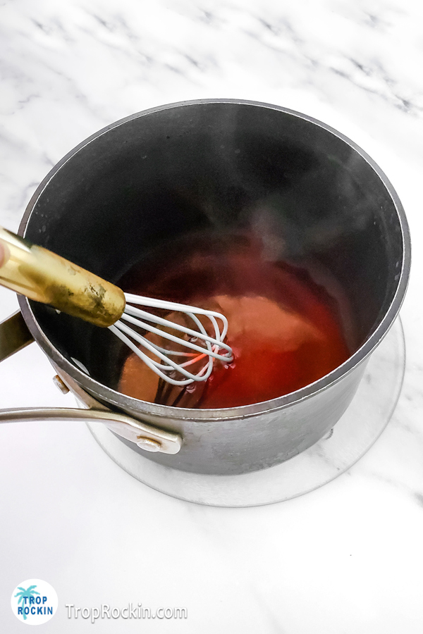 Saucepan with hot water, strawberry jello and a whisk to stir it with.