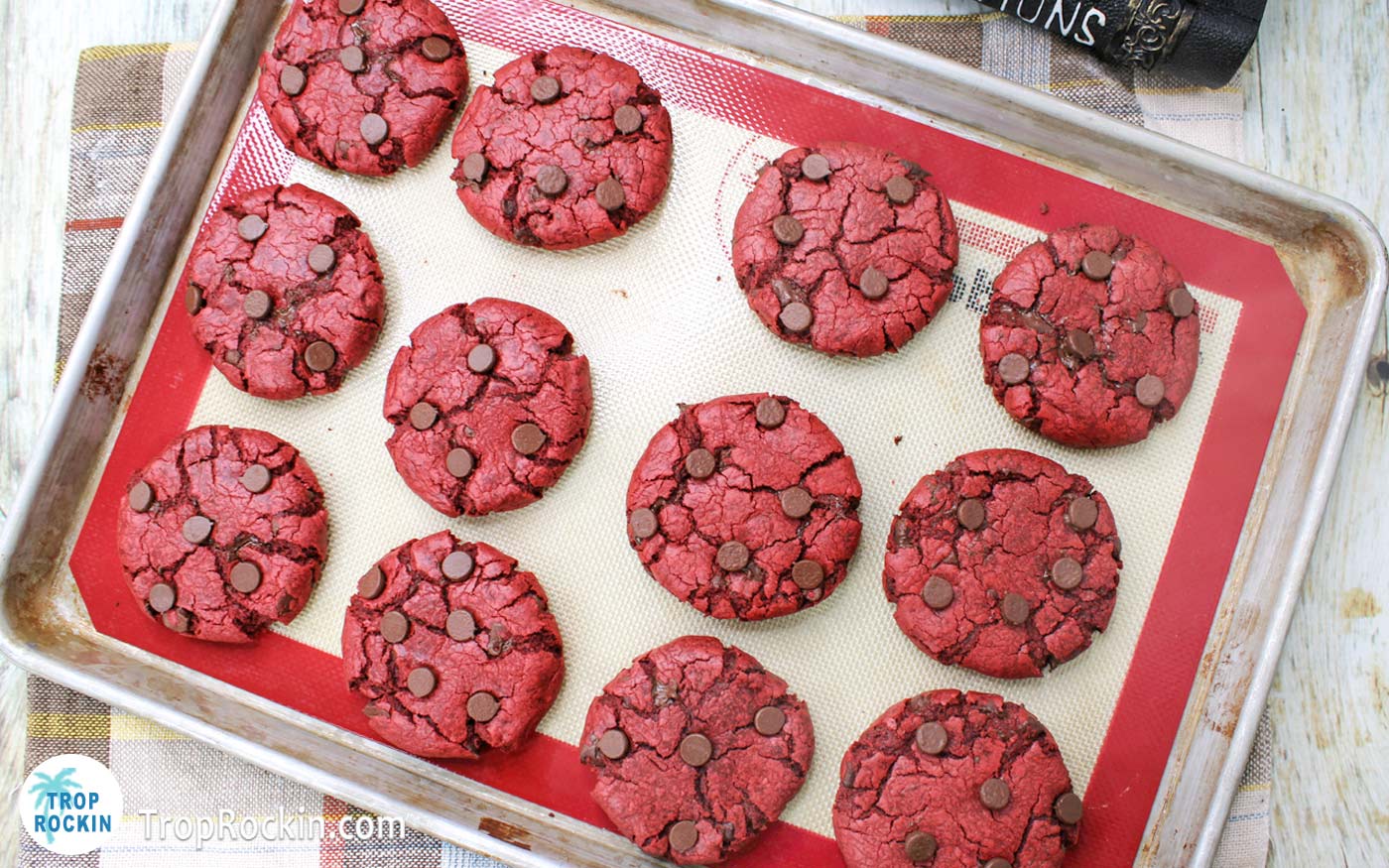 Baked red velvet chocolate chip cookies on baking sheet with silicone mat.