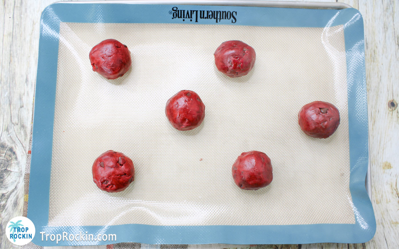 Red velvet chocolate chip cookie dough balls on a cookie sheet with a silicone baking mat.