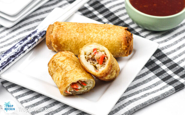 Two cooked air fryer frozen egg rolls on square white plate. One egg roll is cut in half.
