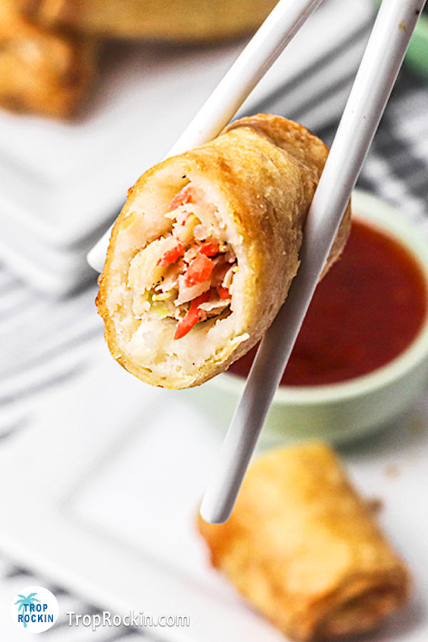 An egg roll cut in half held up by a pair of chopsticks.