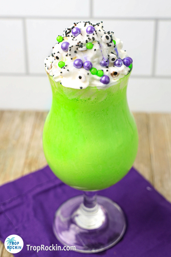 Halloween geen milkshake with whipped cream and sprinkles on a purple napkin.