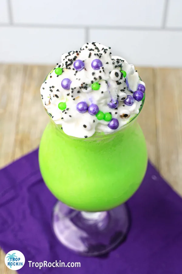 Top view of a green hocus pocus halloween milkshake with whipped cream on top with sprinkles and candy eyes on top.