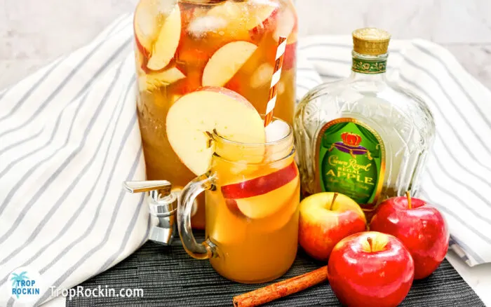 Apple Cider Whiskey Punch in a mason jar with an apple crown bottle and a ull pitcher of punch in the background.