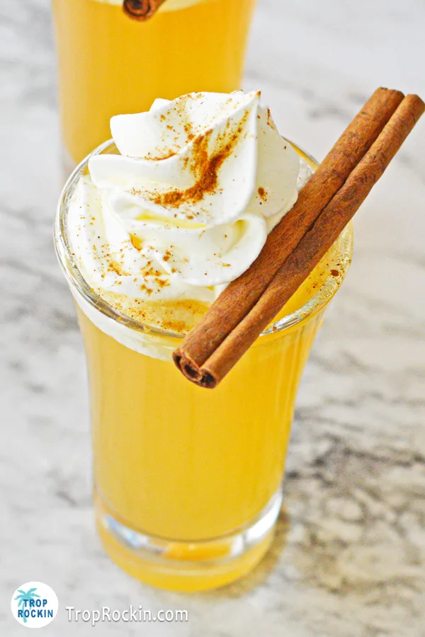 Close up of one apple pie shot with an angled top view to showcase the whipped cream, cinnamon sprinkles and cinnamon stick.