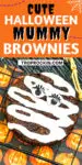 Halloween Mummy Brownie upclose with white icing and cute candy eyes with lashes. Text overlay with recipe title for sharing to social media.