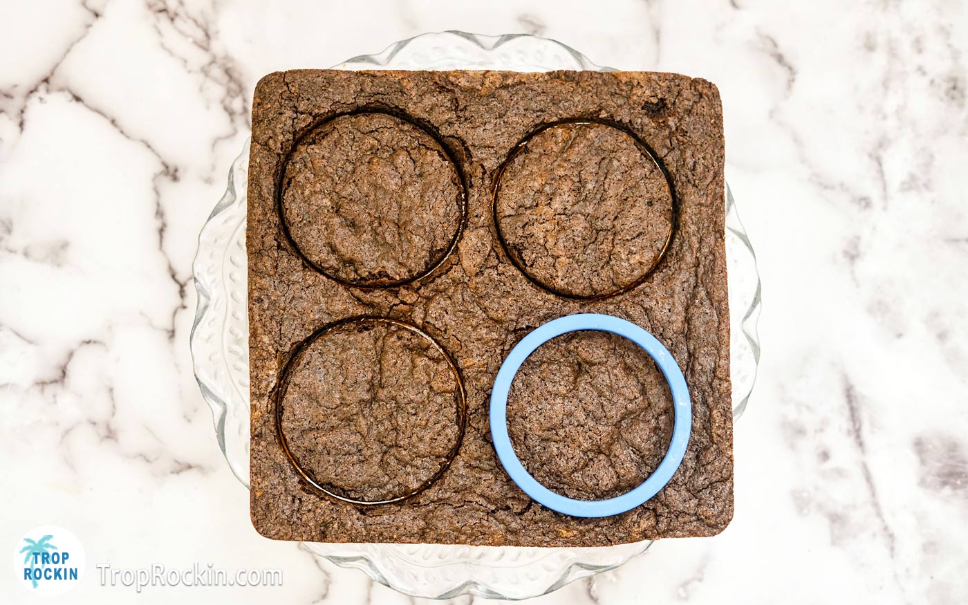 Brownies removed from square baking pan with a round cookie cutter on top cutting the brownies into circles.