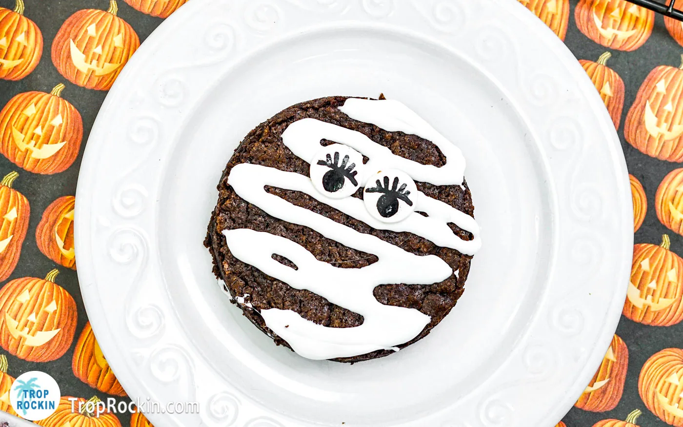 Halloween mummy brownie on a white plate with a Halloween theme background.