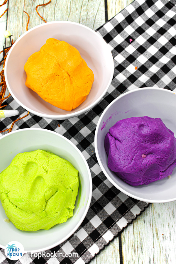 Three bowls of dough with food dye mixed in. One purple, one green and one orange.