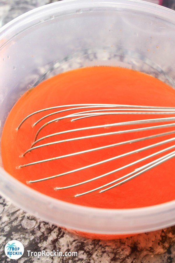 Orange jello mixed with hot water in a large bowl with a whisk.