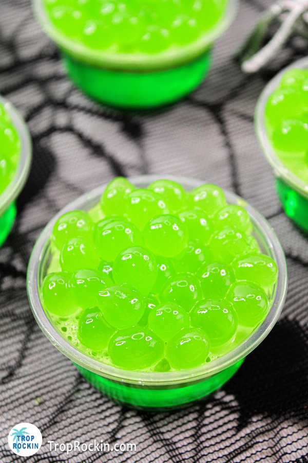 Top view of a single witches brew halloween jello shot with bright green popping boba on top.