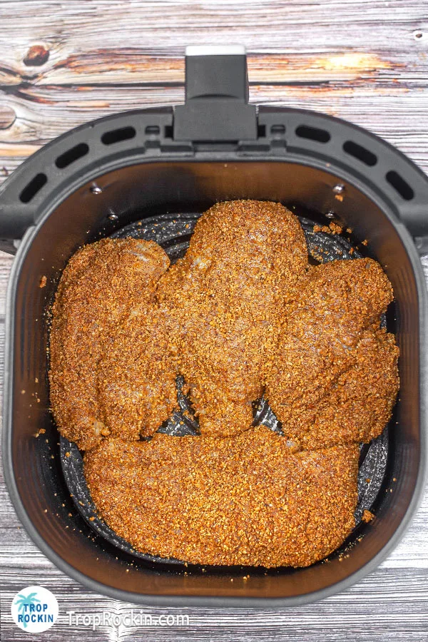 Four almond coated chicken breasts in the air fryer basket.