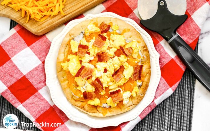 Air fryer breakfast pizza on a white plate with red checkered napkin underneath.
