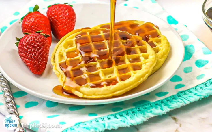 Two Air Fryer Frozen Waffles on a plate with strawberries and syrup pouring on top.