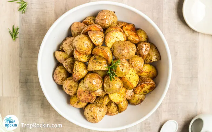 A bowl of rosemary air fryer potatoes on a wooden background.