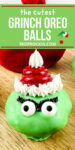 Close of Grinch Oreo Ball decorated with The Grinch face and red santa hat on top. Text overlay of the recipe title for sharing to social media.