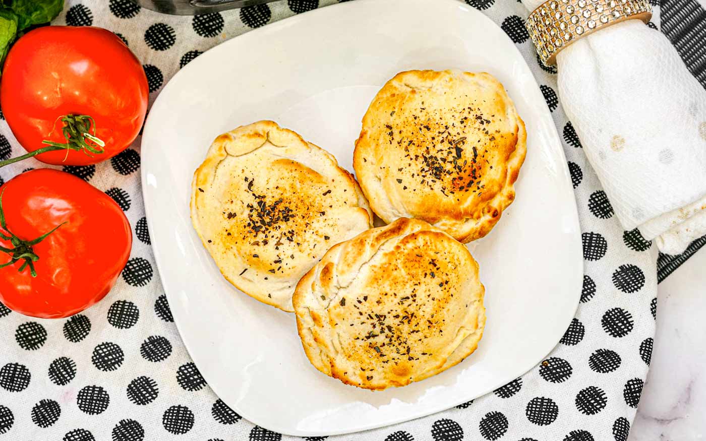 Three air fryer pizza bombs made from biscuits on a white plate.