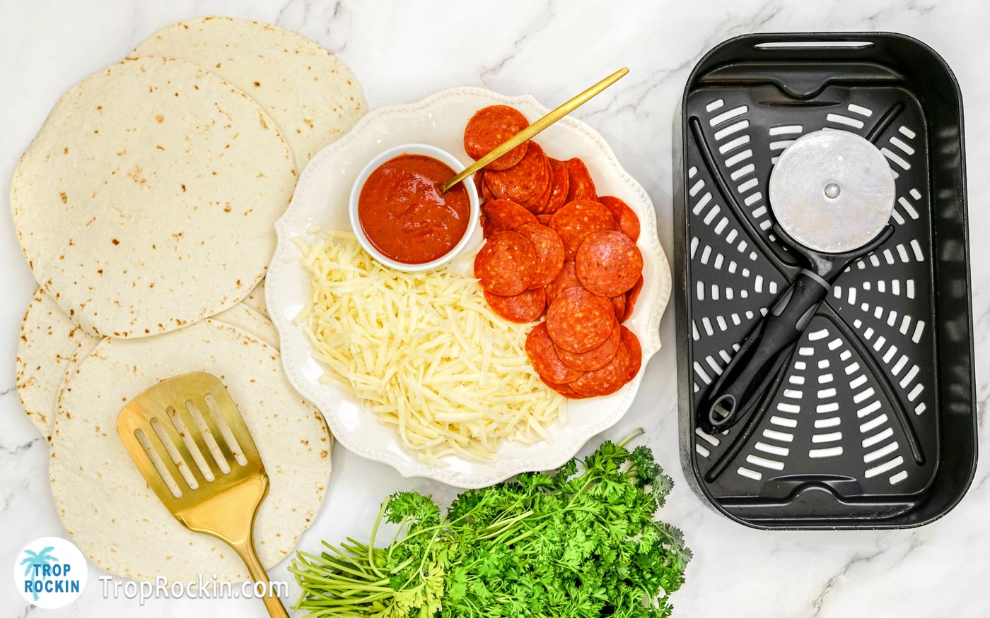 Tortilla pizza ingredients displayed on counter top next to an air fryer basket.